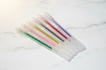 7 glitter gel pens with clear sparkly barrels in green, pink, gold, silver, red, orange and lavender on marble desk