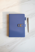 Periwinkle blue faux leather journal with silver clasp on marble desk